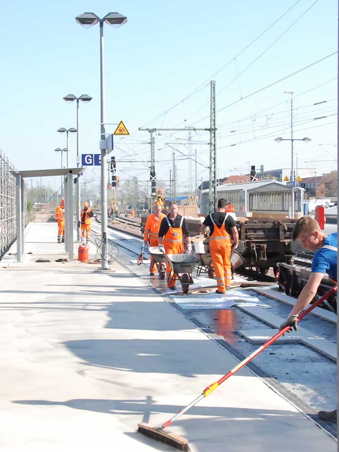 Arbeiter asphaltieren einen Bahsteig mit weißem Asphalt.