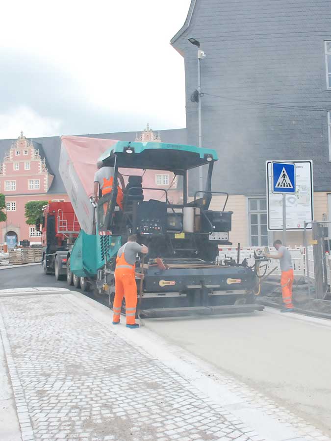 Asphaltfertiger bringt beigen Asphalt in Innenstadt auf.